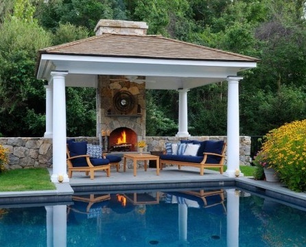 The classic-style barbecue gazebo is located amid decorative trees and flowers reflected in the smooth surface of the pool.