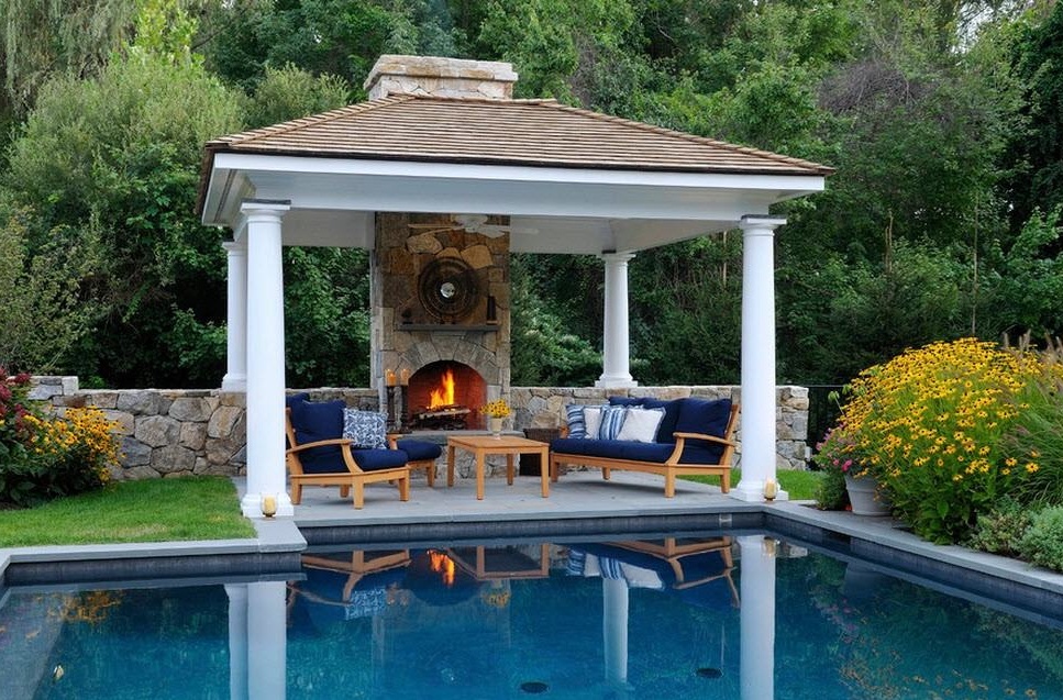 Il gazebo barbecue in stile classico si trova tra alberi decorativi e fiori riflessi sulla superficie liscia della piscina.