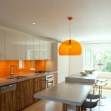 Oranžinė prijuostė ir pakabukas lempa šviesios virtuvės interjere