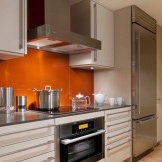 Orangefarbene Schürze kombiniert mit Weiß- und Grautönen im Innenraum der Küche