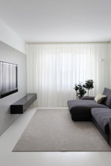 Sofa hitam di ruang tamu putih dengan gaya minimalis